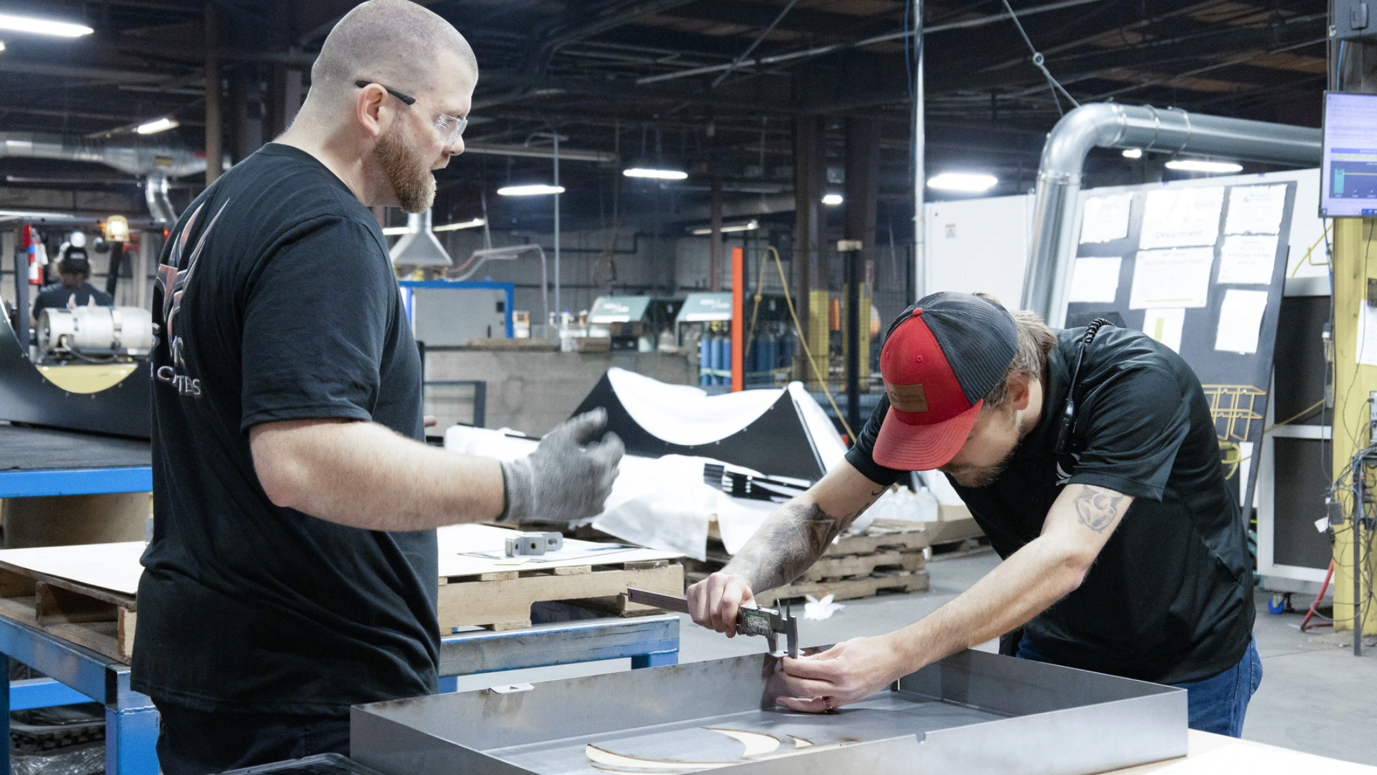 Workers collaborate on precise metal fabrication in a busy manufacturing facility.