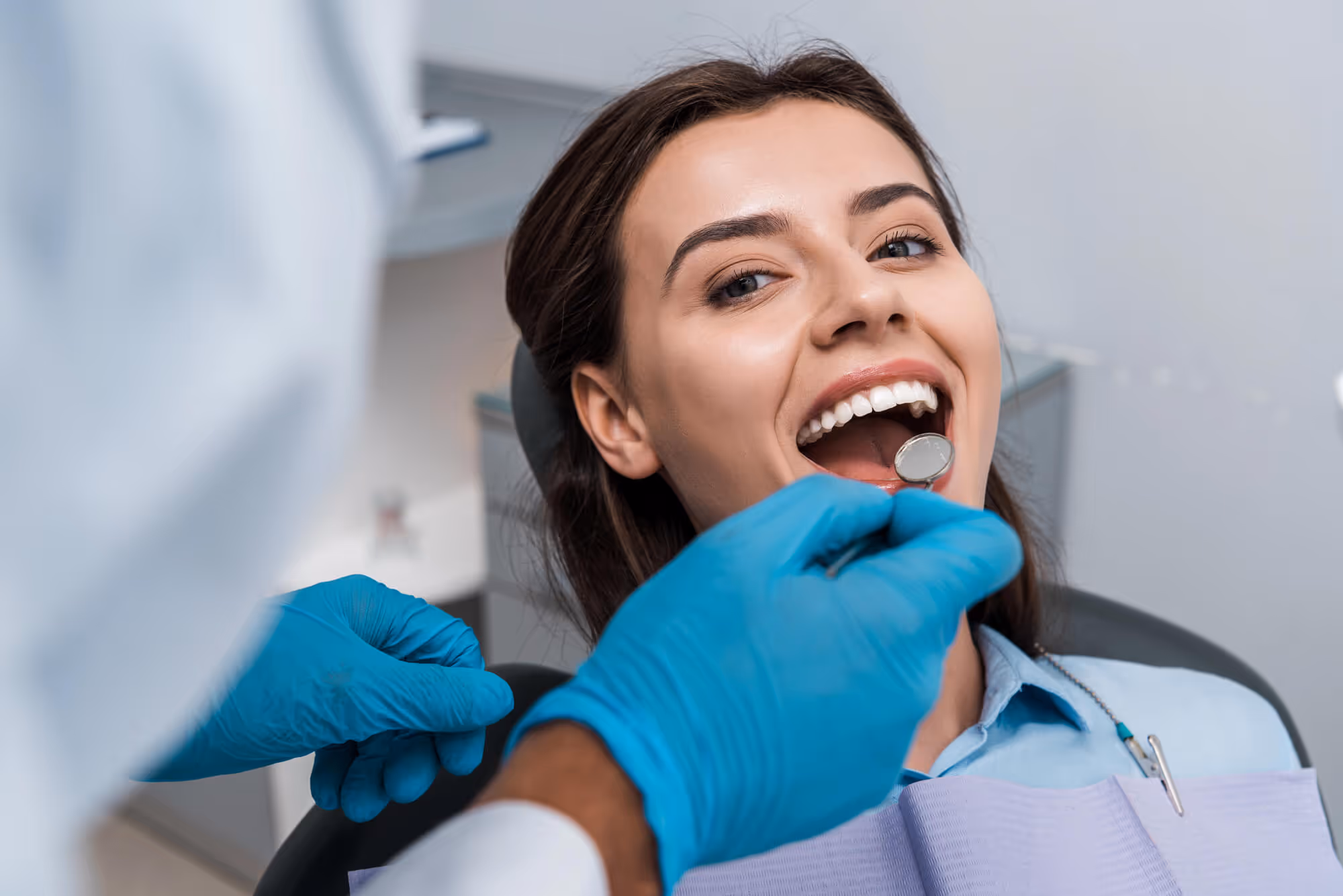 Patient smiling with mouth open during dental exam by dentist wearing blue gloves.