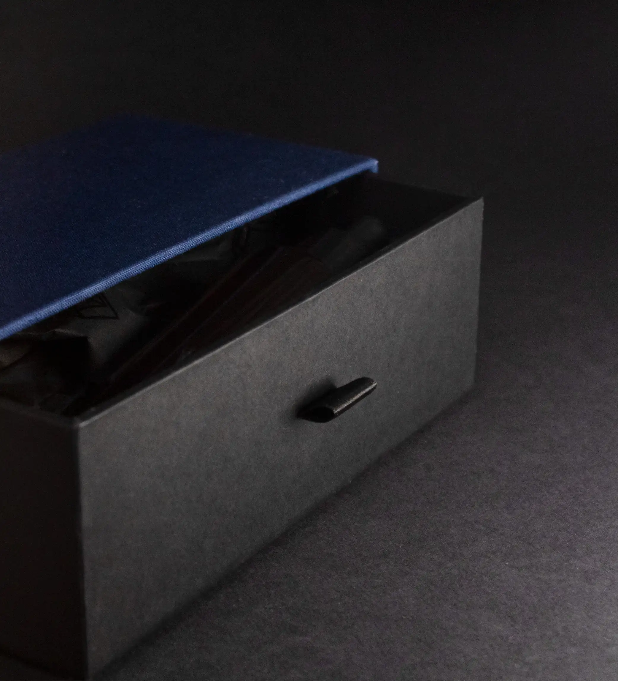 Boîte tiroir noire entrouverte, languette de tirage et ouvrage relié bleu à l'intérieur