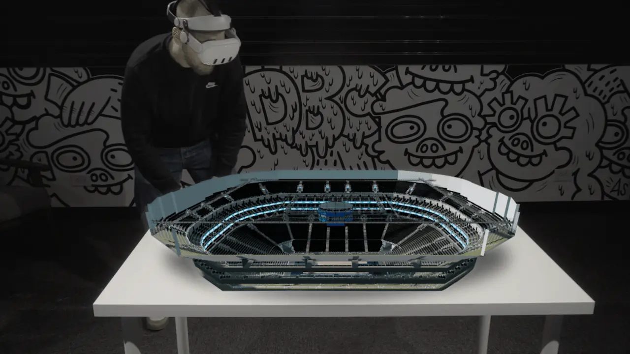 Person wearing a VR headset interacting with a 3D virtual stadium model on a white table.