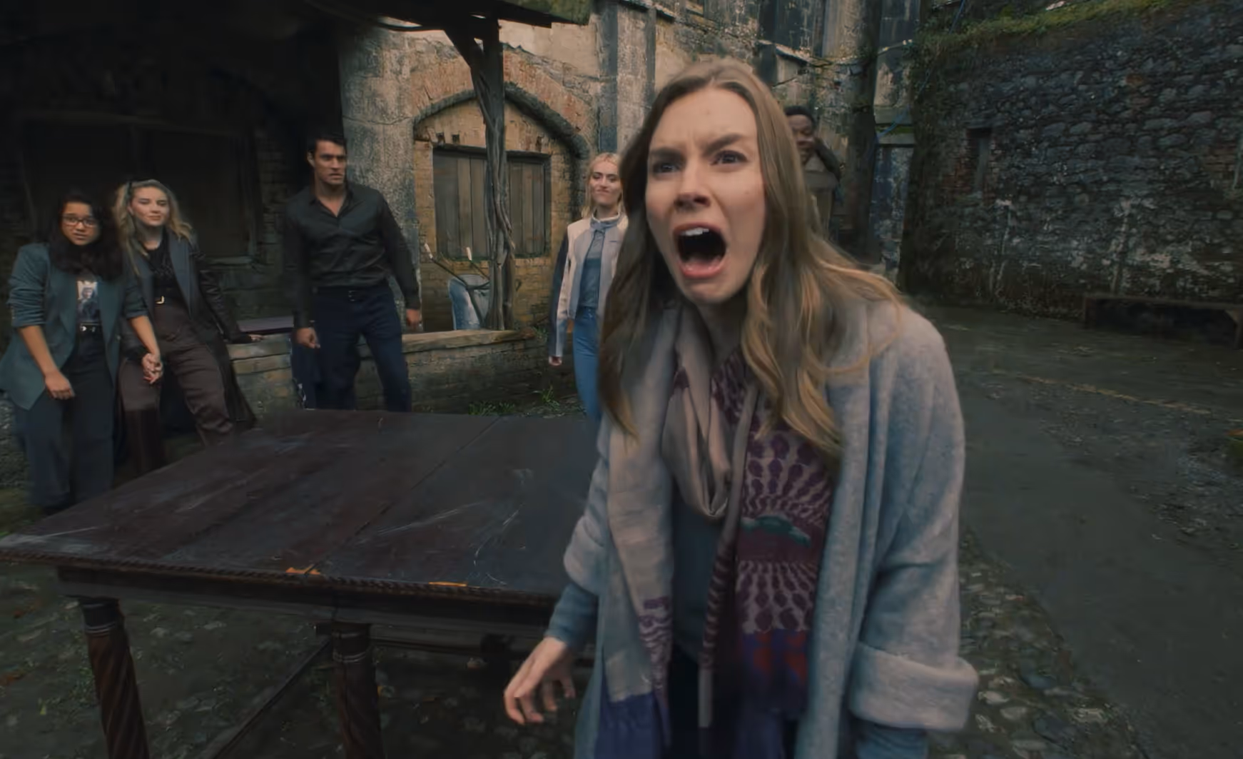 A woman in a scarf and coat screaming with four people standing behind her near an old stone building.