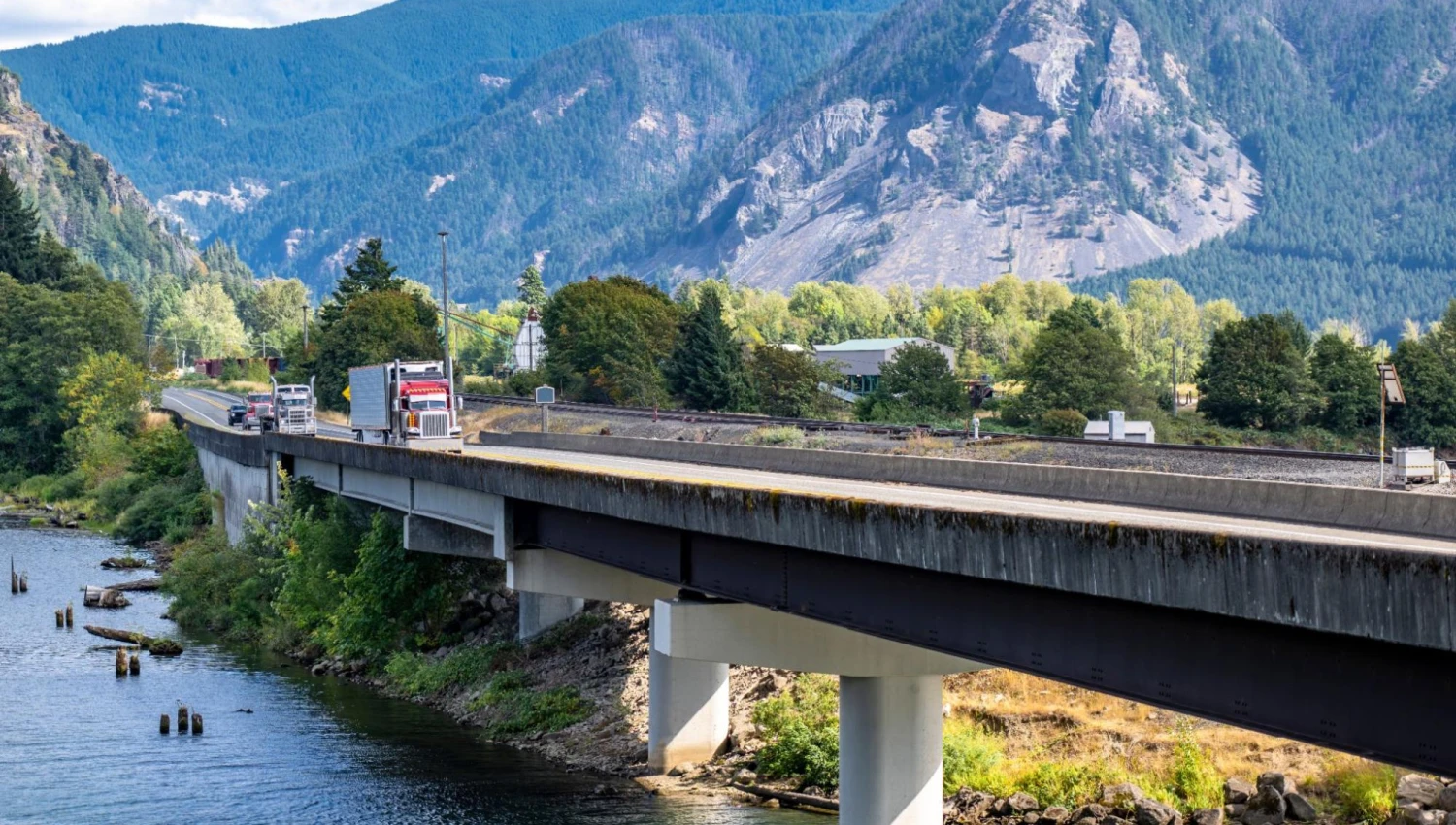 A truck in the distance on a bridge on a beautiful day in the mountains.