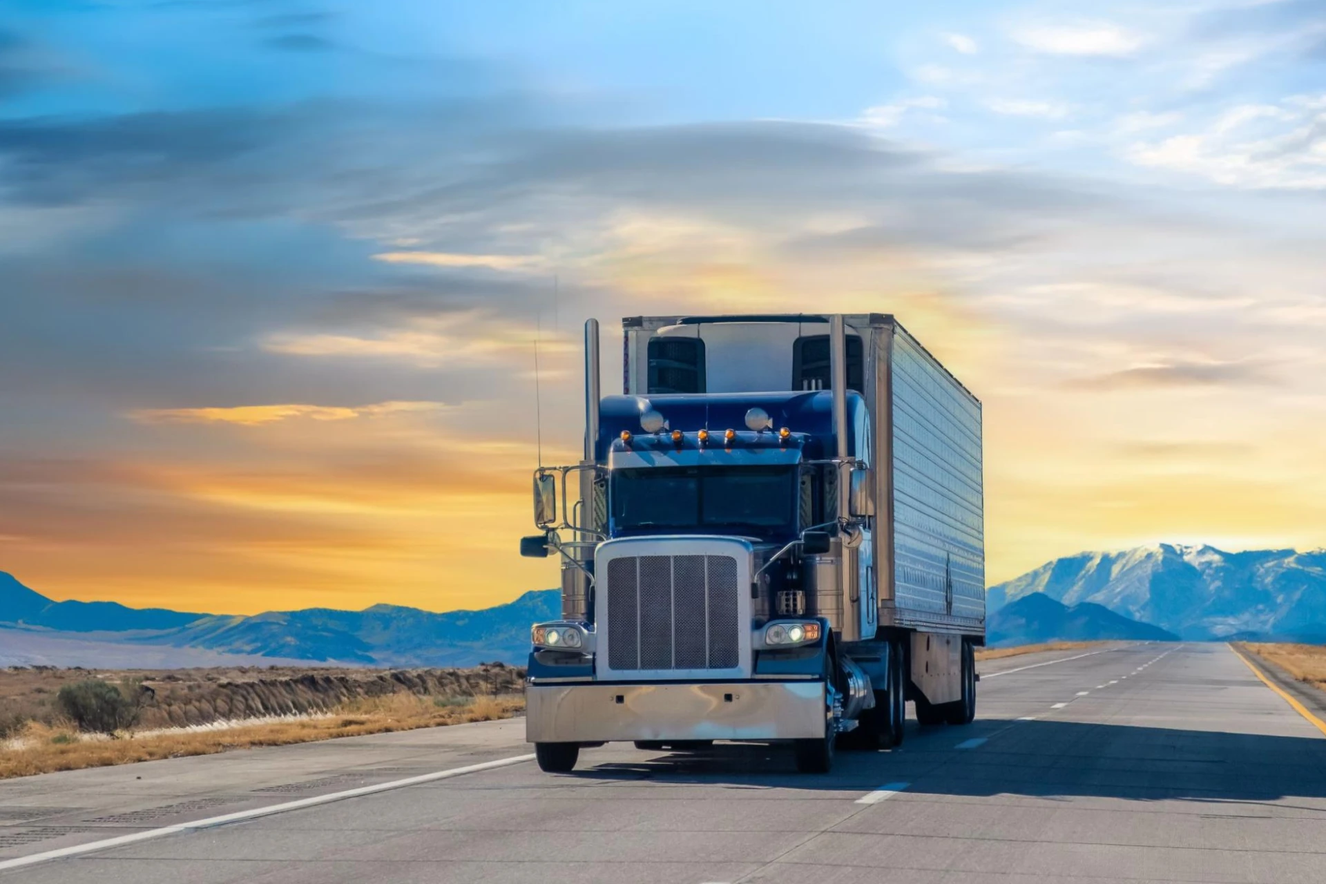 A semi-truck driving on a road surrounded by mountains