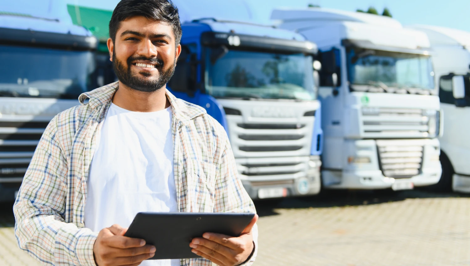 Smiling fleet manager holding a tablet in front of parked commercial trucks
