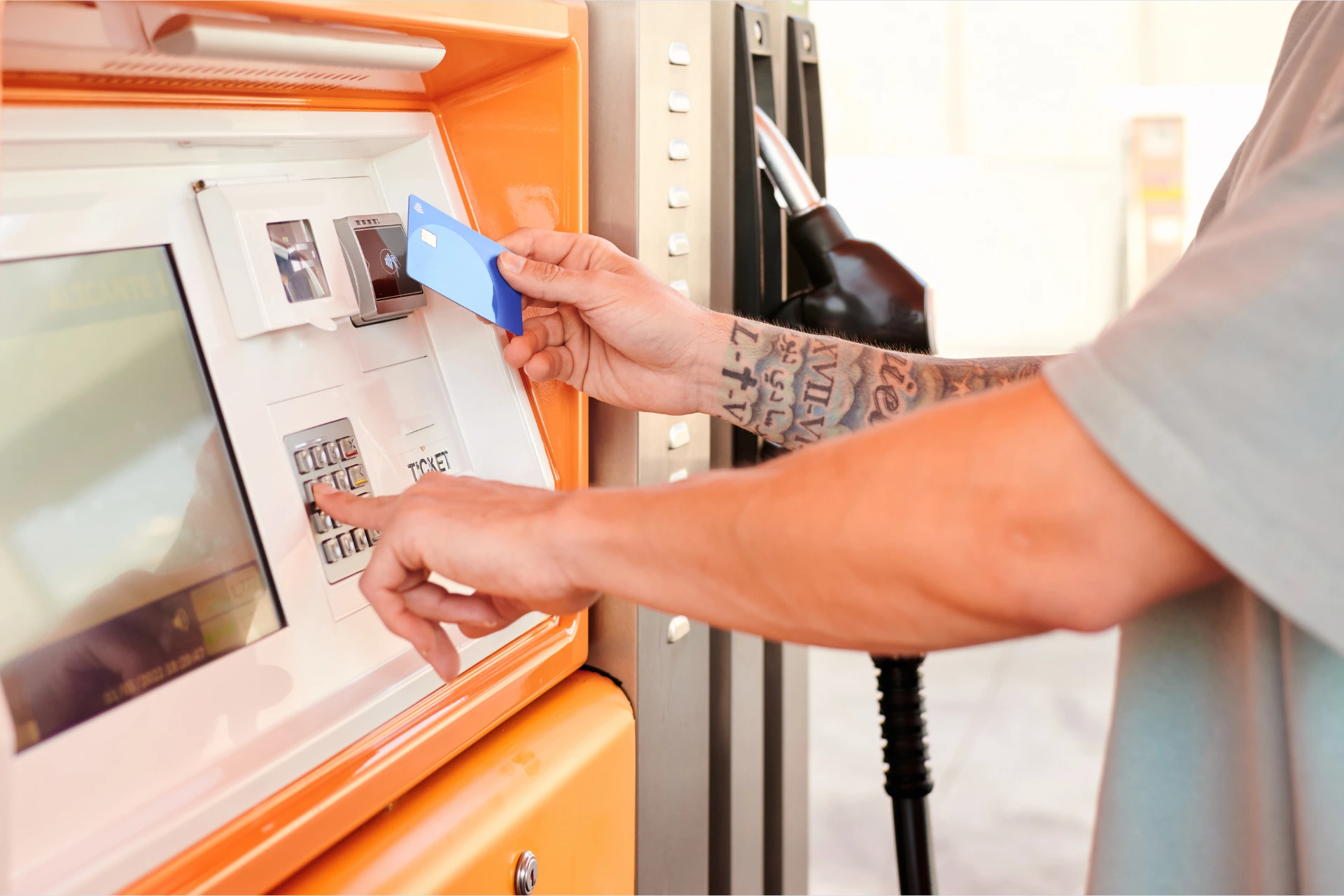 A tattooed arm taps a blue fuel card into a fuel station’s automated payment system
