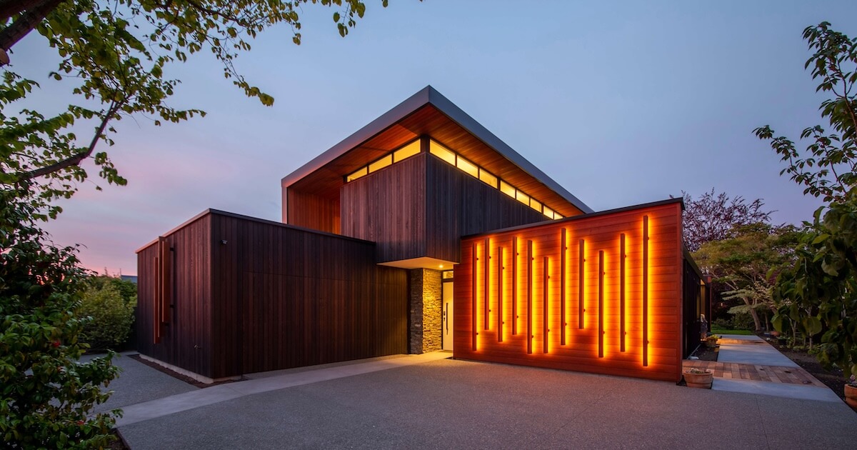 Modern house with dark wood exterior and vertical orange illuminated light strips at dusk.