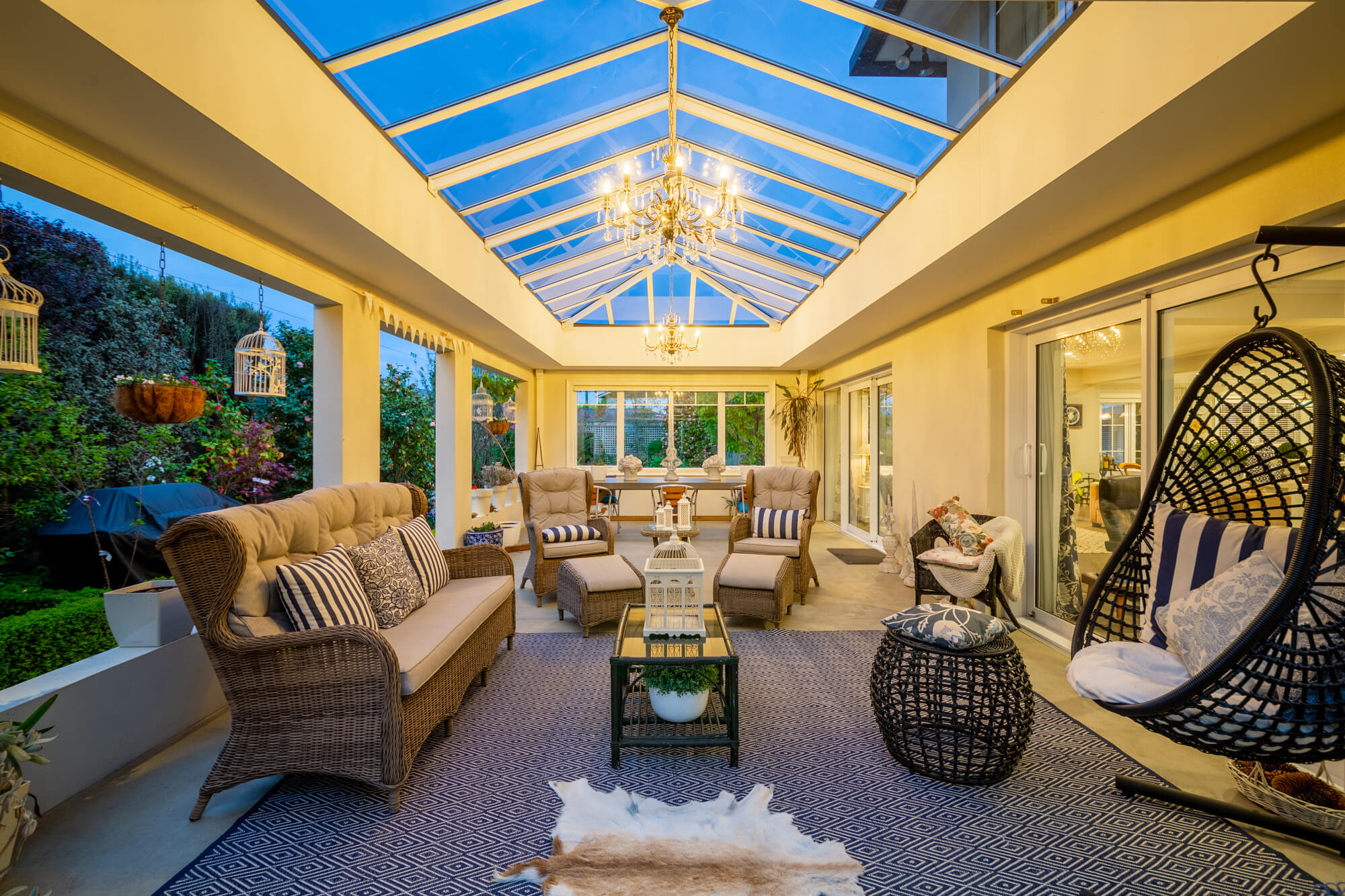 Cozy sunroom with a glass ceiling, wicker sofa and chairs, a hanging chair, and a patterned rug.