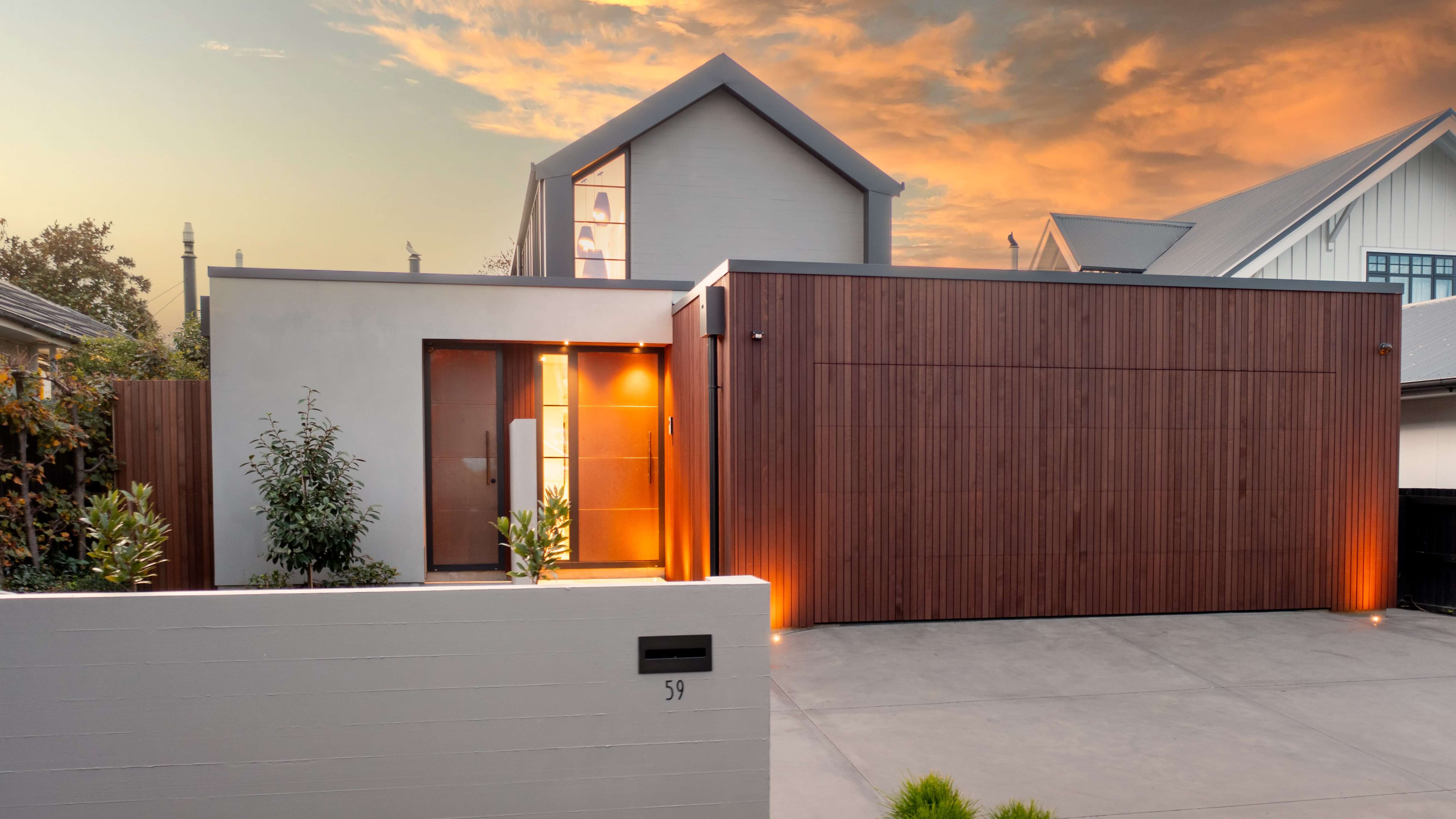 Modern house with a wooden garage door and illuminated entrance at sunset.