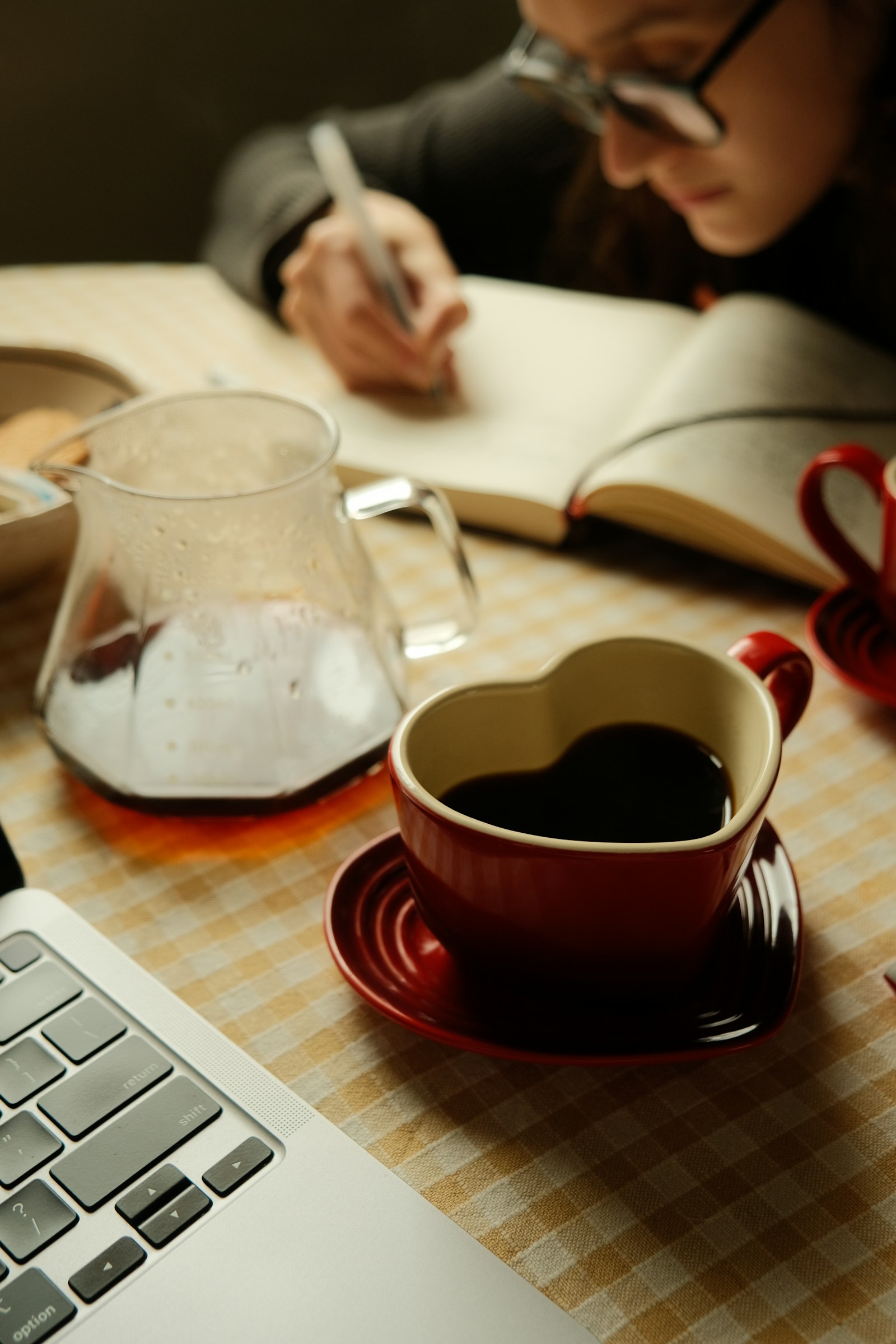 Person som skriver i en anteckningsbok bredvid laptop och kaffe