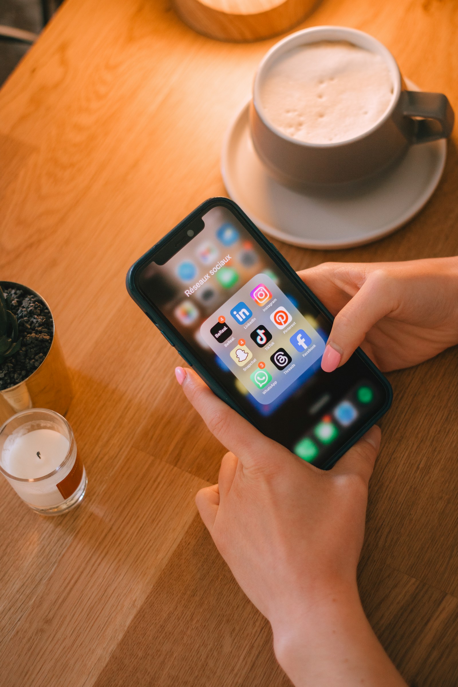 Hand som håller en mobil med appar bredvid en kaffekopp