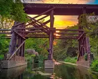 Sunset illuminates a rustic wooden bridge over a calm river, surrounded by lush greenery and tranquil waters in Cedar Park Texas.