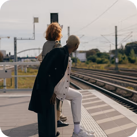 a man and woman standing on a platform next to train tracks