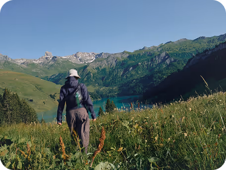 a person walking in a grassy field with mountains in the background