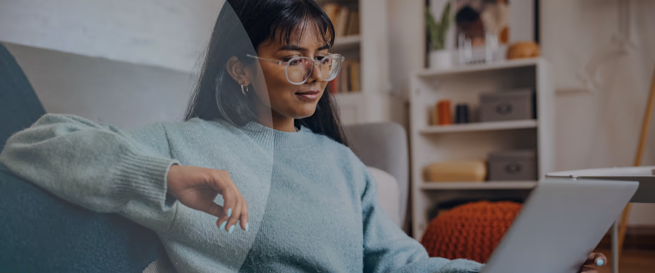 Woman with long dark hair and clear glasses wearing a light blue sweater, looking down and smiling.