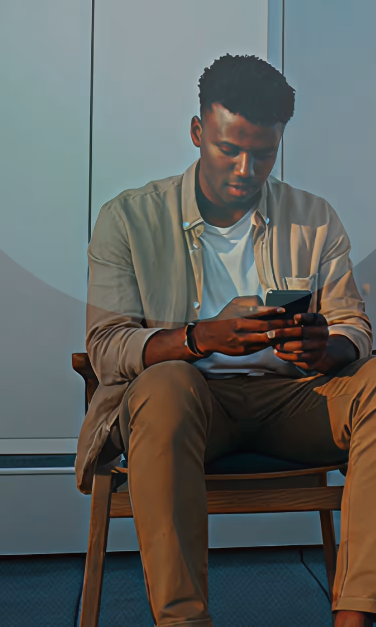 Young man sitting on a chair indoors, looking at and using his smartphone.