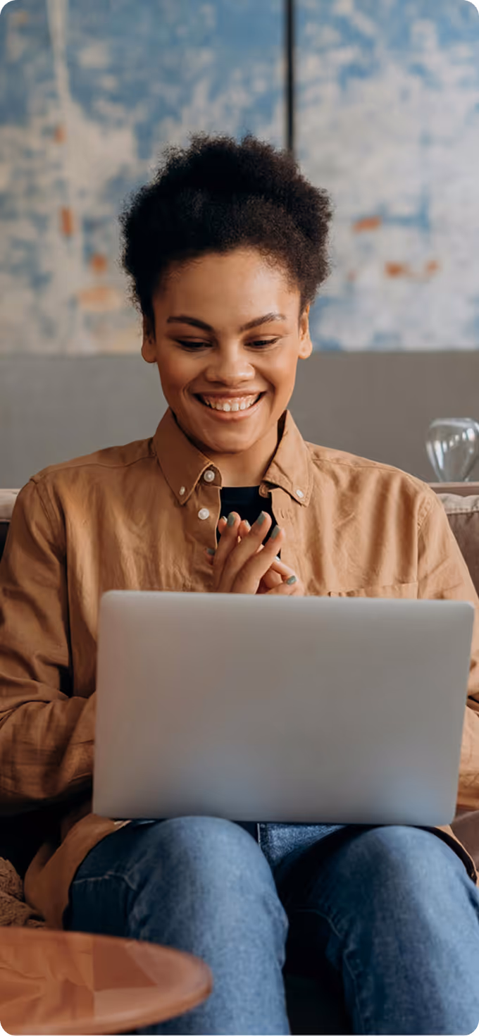 Smiling woman sitting on a couch using a laptop in a cozy living room.