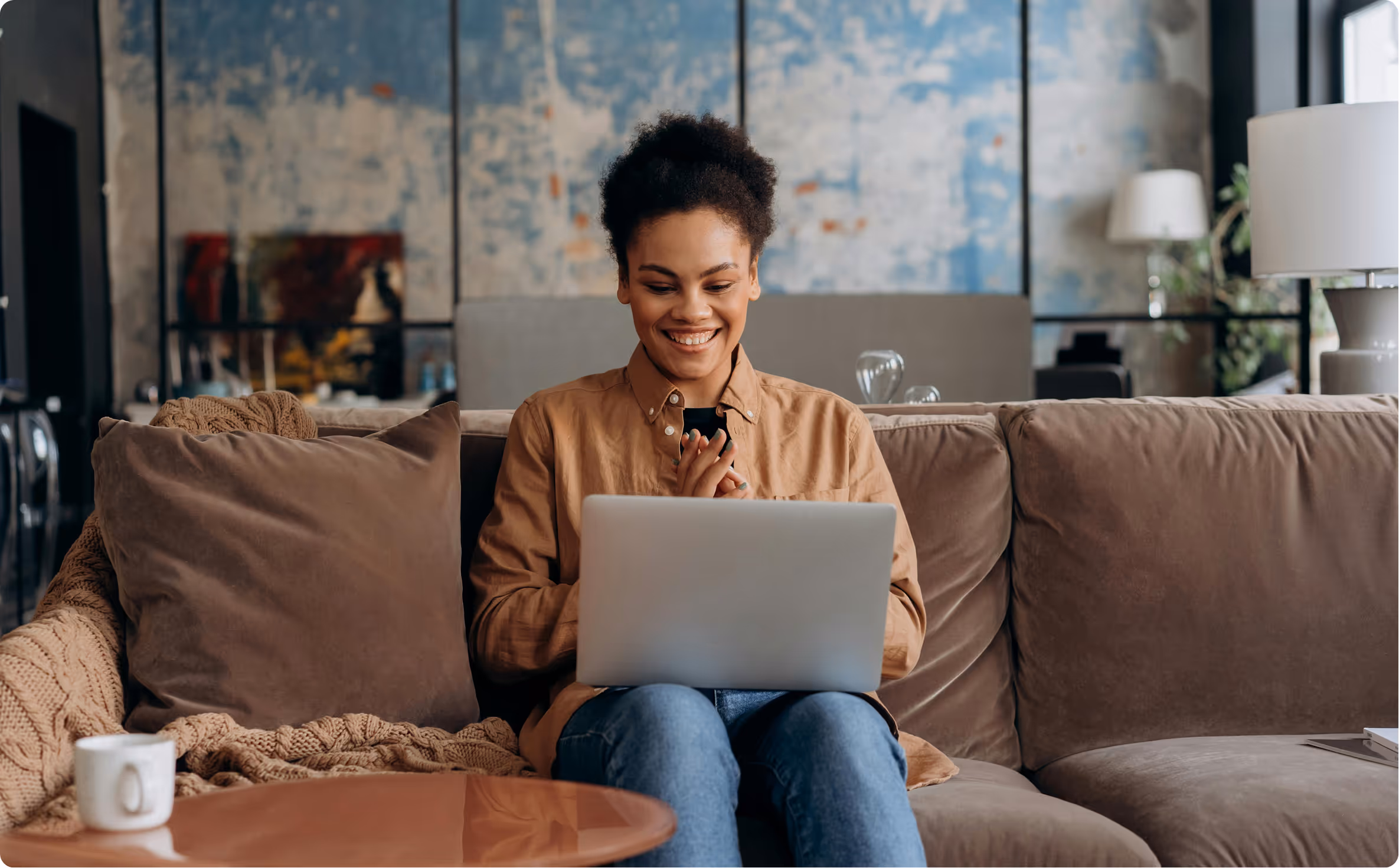 Smiling woman sitting on a couch using a laptop in a cozy living room.