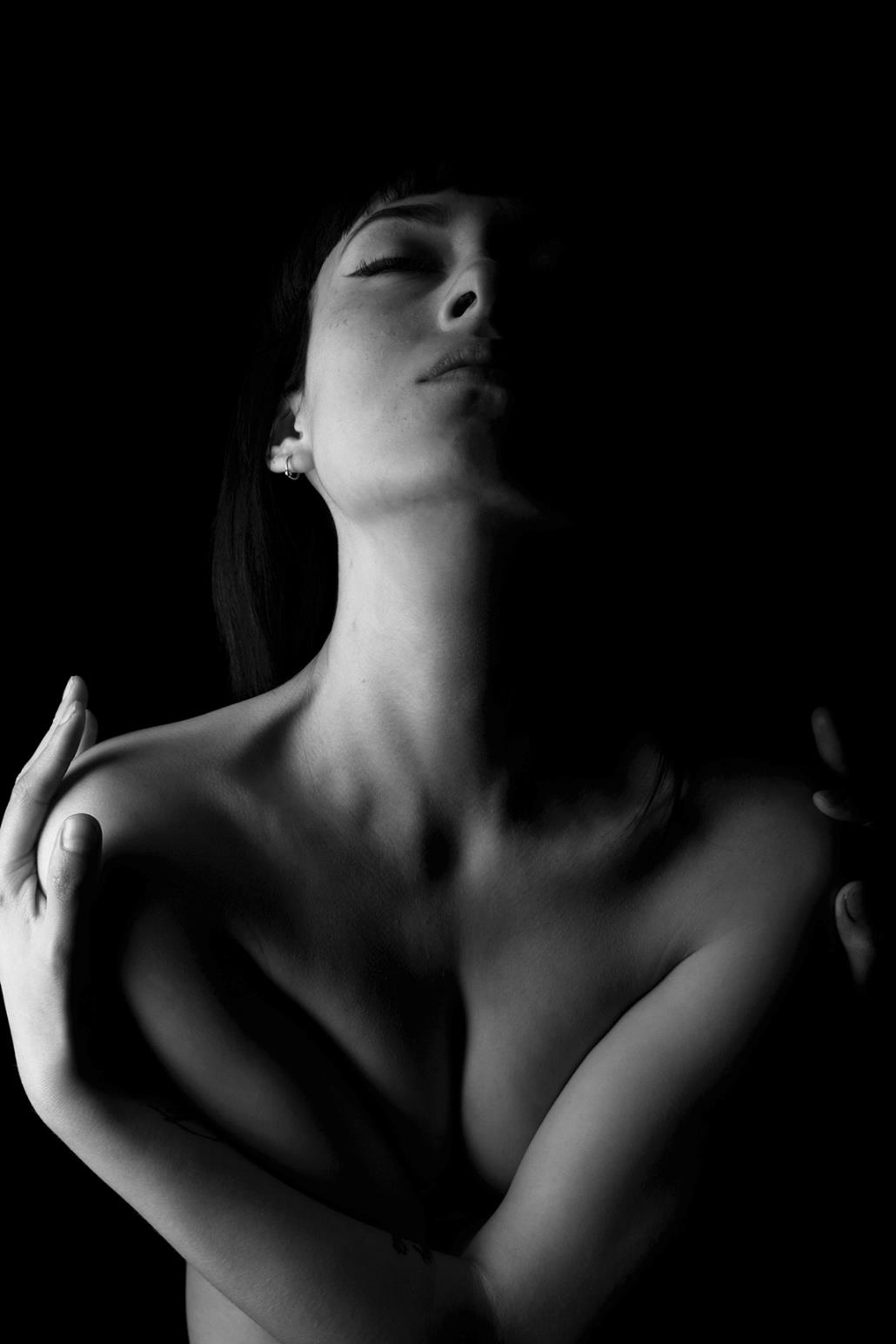 Retrato artístico en blanco y negro de una mujer con iluminación dramática, cabeza inclinada hacia atrás y brazos cruzados sobre el pecho desnudo.