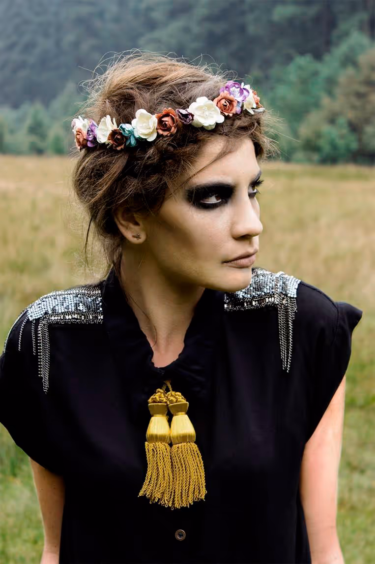 Modelo en un paisaje natural, con corona de flores y retoque oscuro en los ojos mirando hacía su lado izquierdo
