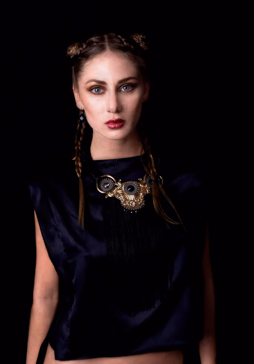 Modelo viendo a la cámara con fondo oscuro, blusa azul y dije en el cuello