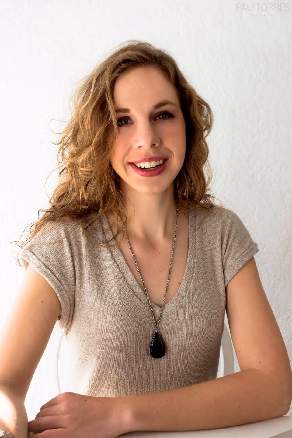 Fotografía de retrato de mujer sonriendo a la cámara con fondo de pared blanca.