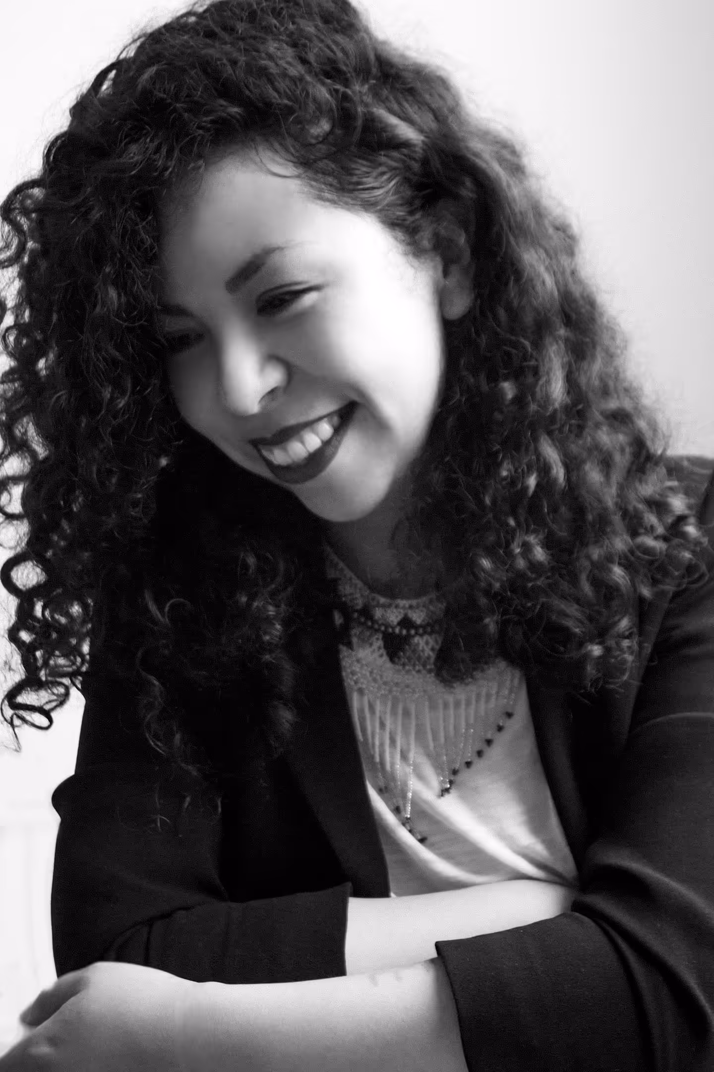 Fotografía blanco y negro de retrato de mujer sonriendo hacía el piso, con fondo de pared blanca.