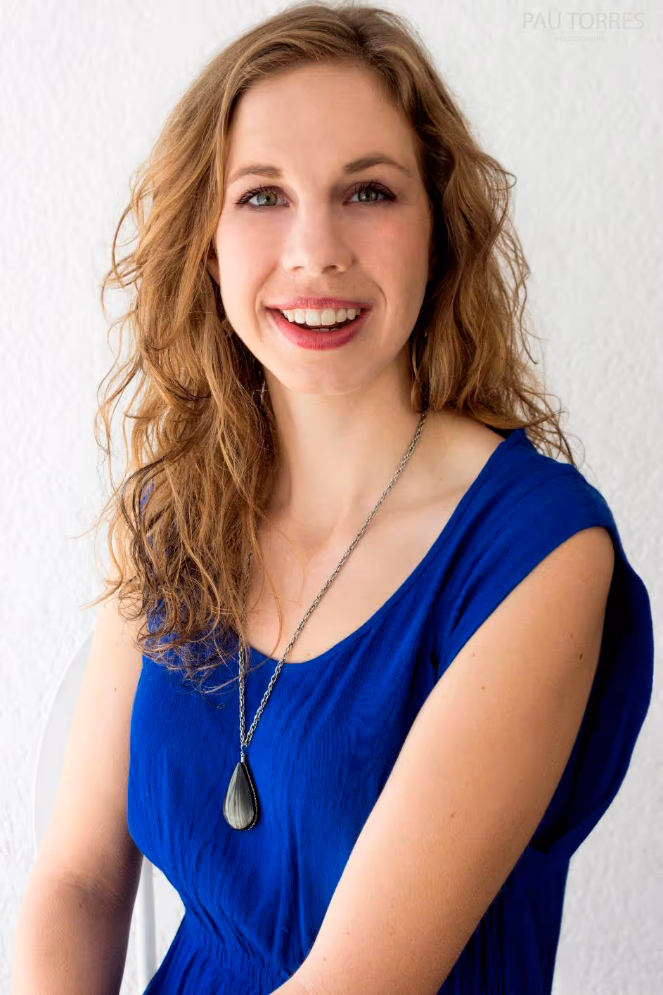 Fotografía de retrato de mujer sonriendo a la cámara con fondo de pared blanca.