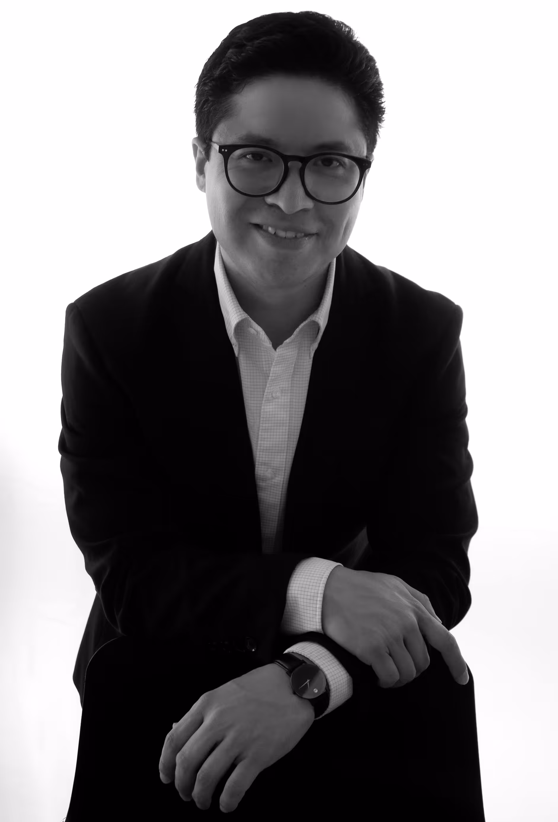 Fotografía blanco y negro de retrato de hombre sonriendo a la cámara con fondo de pared blanca.