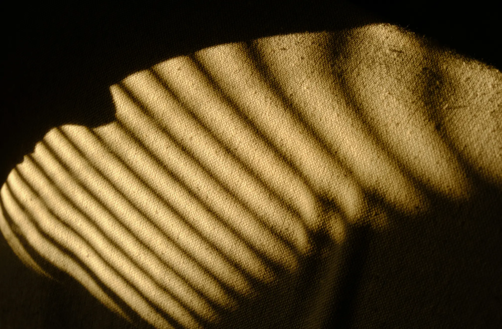 Shadow of blinds cast in parallel lines on a textured beige fabric surface.