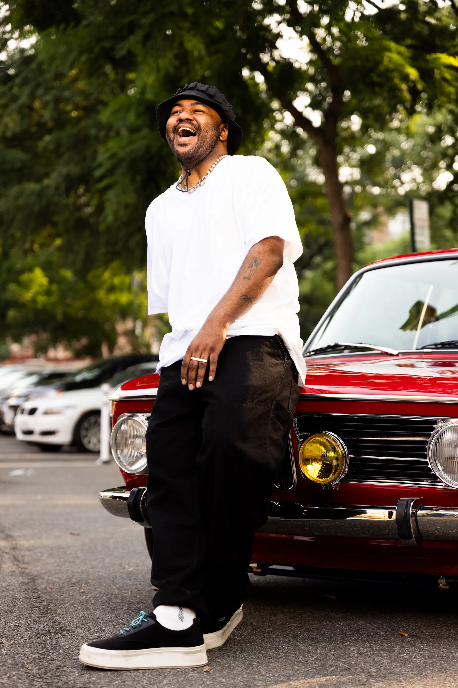 Model posing in front of vintage BMW wearing Hanes white tee for “50 Years of Hip-Hop” campaign — So & So Productions fashion photography.