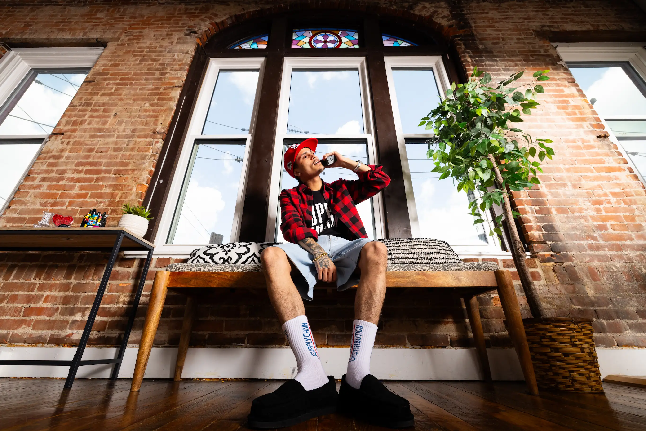 Model sitting by apartment window in Supply Chain Distro streetwear outfit — So & So Productions natural light photography.