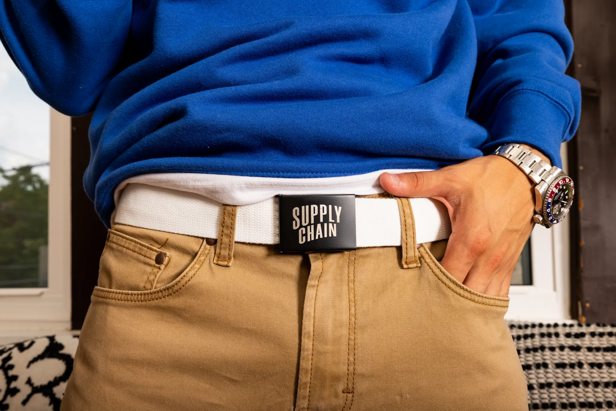 Close-up of Supply Chain Distro belt and buckle detail as model poses by window — So & So Productions apparel photo.