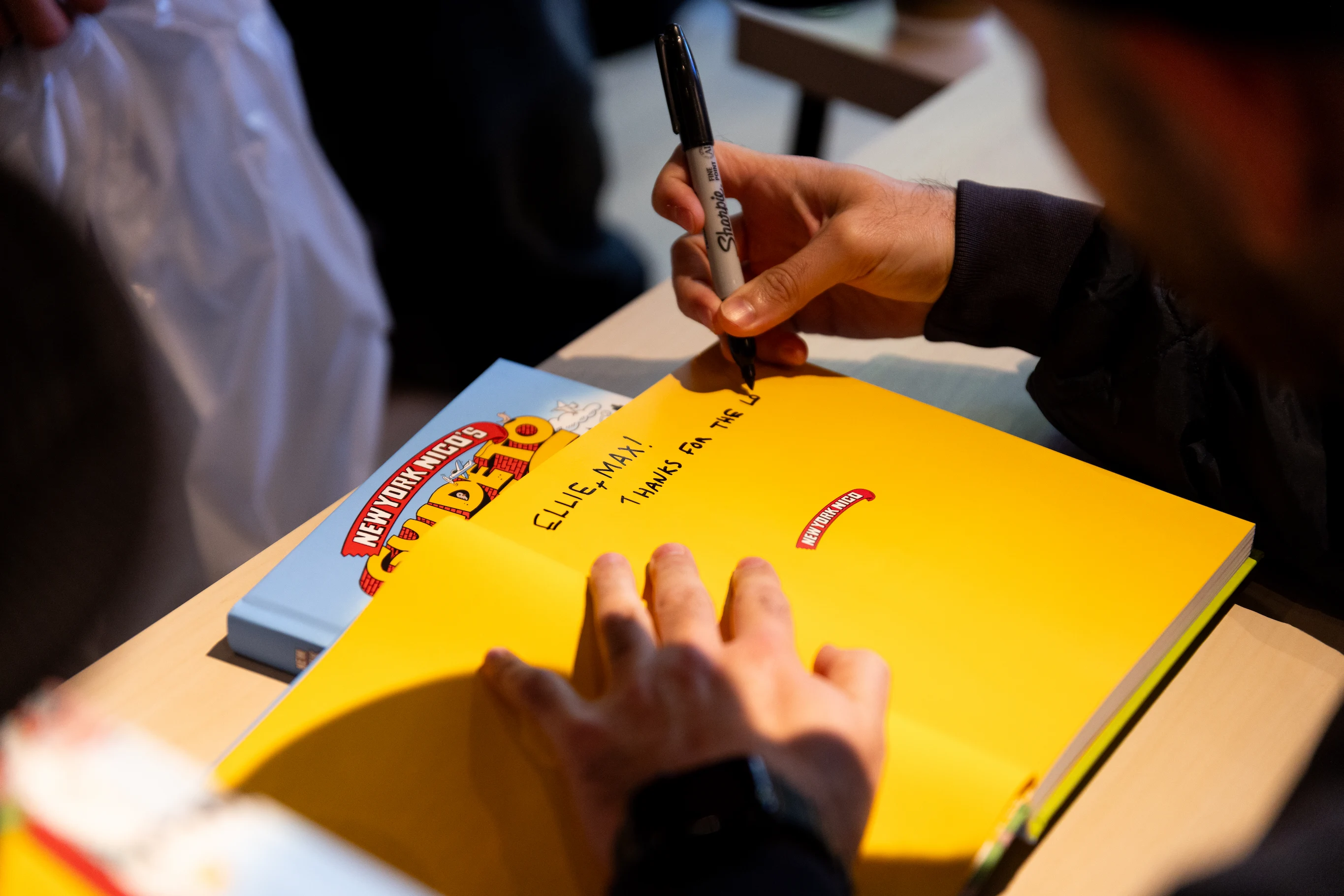 Detail photo of New York Nico autographing a book cover — So & So Productions cultural documentation.