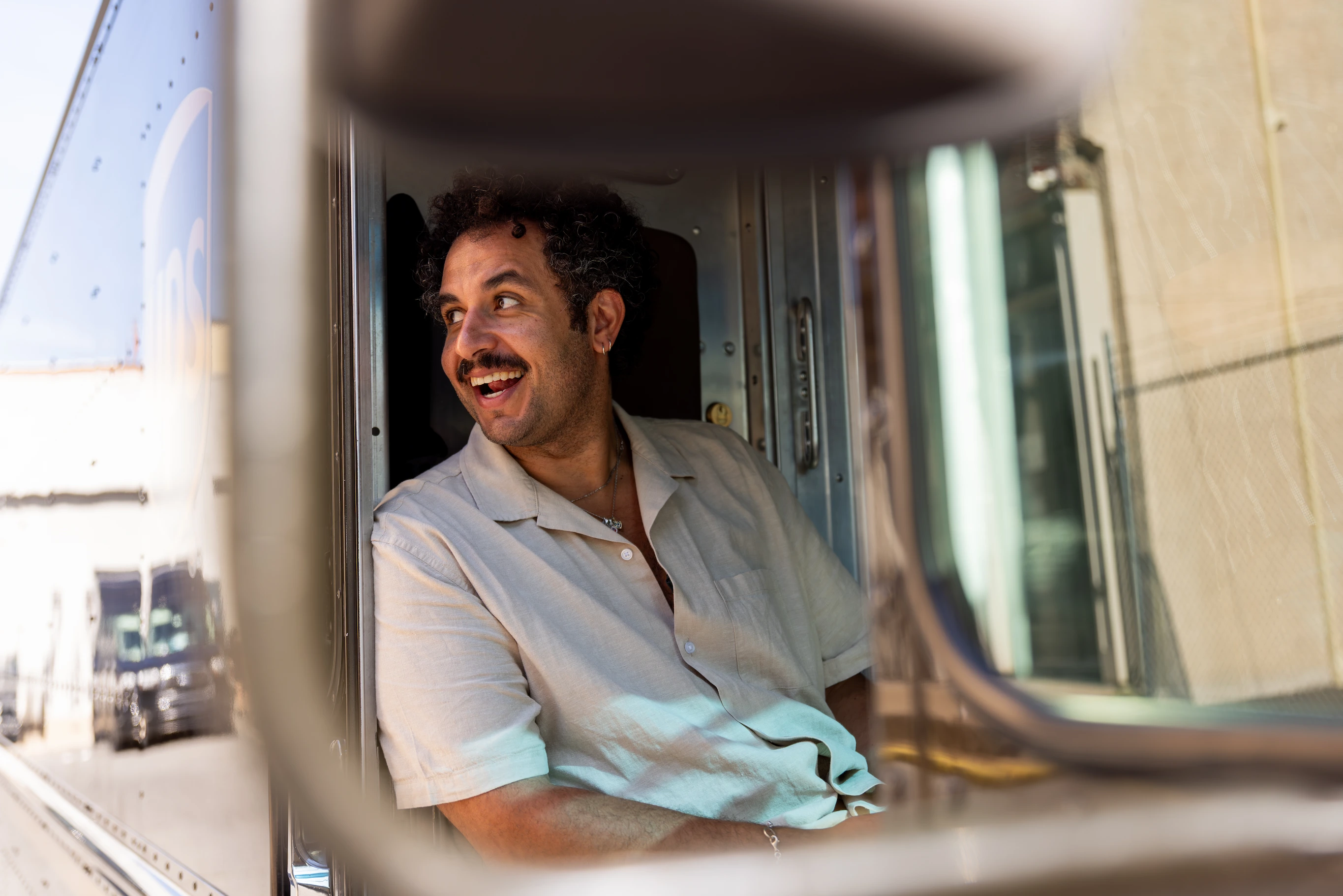Kareem Rahma sitting inside UPS delivery truck cabin with driver, window open city street — So & So Productions storytelling photograph