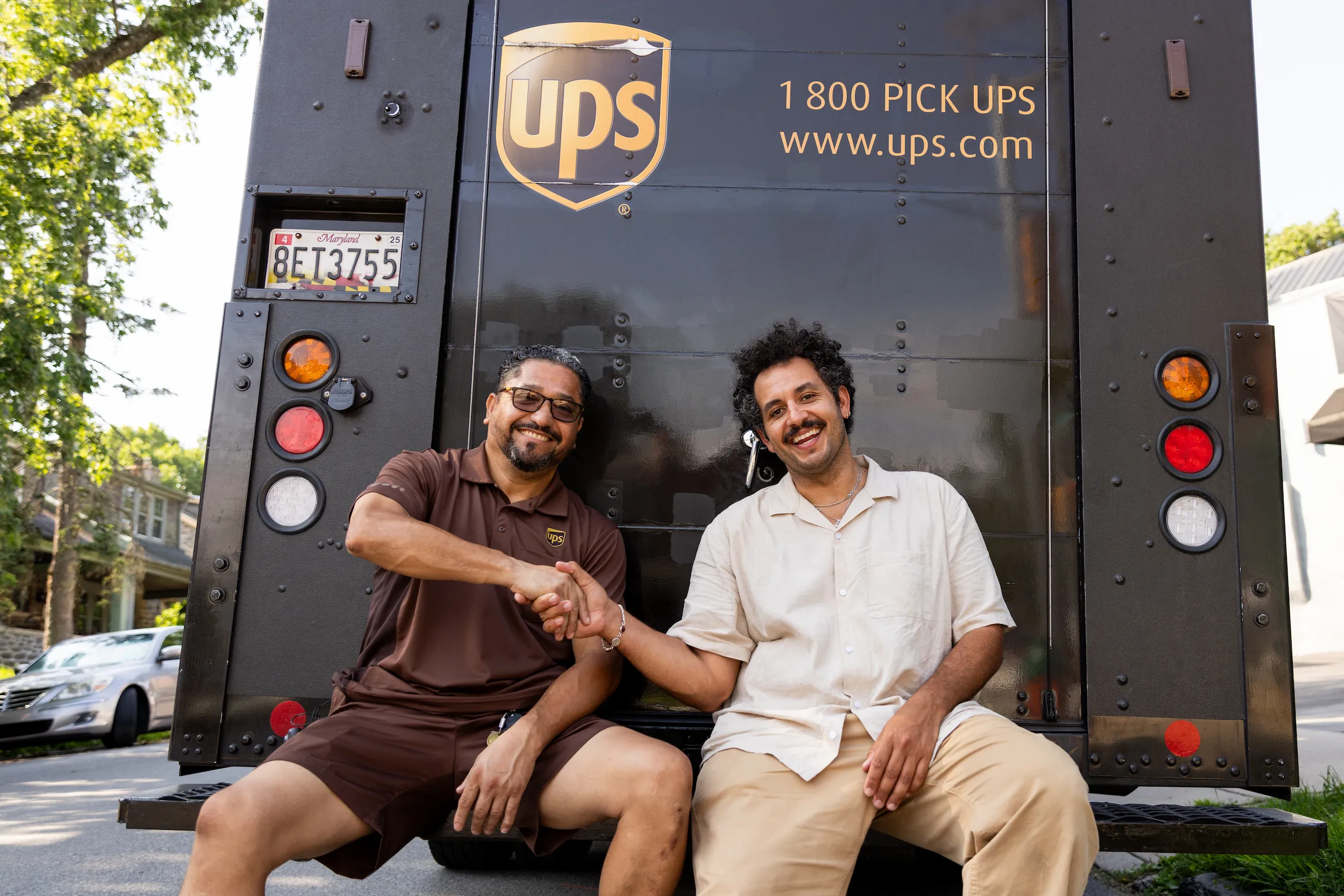 Kareem Rahma sitting with a UPS driver in brown uniform during Business Trips shoot — So & So Productions photo
