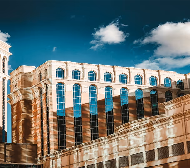 Modern building with large vertical windows reflecting the sky and clouds under a blue sky with scattered clouds.