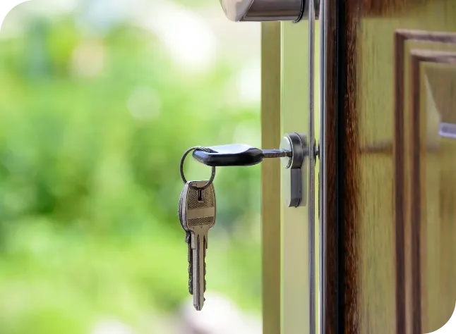 Metal keys hanging from a key inserted in a door lock with a blurred green background.
