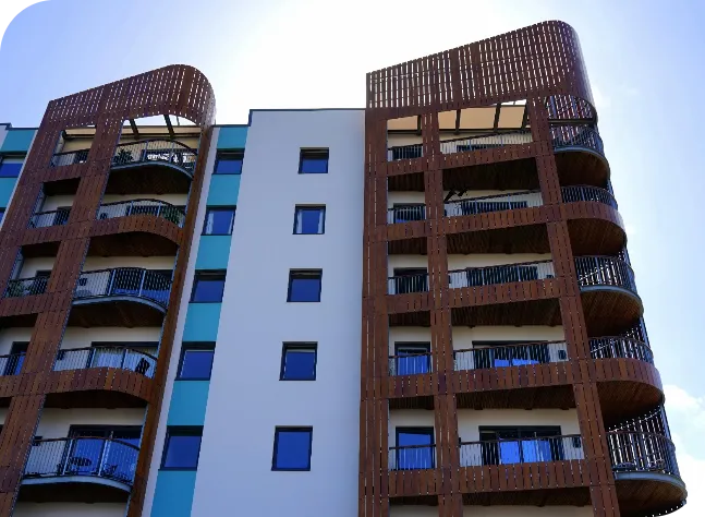 Modern apartment building with curved wooden balconies and blue-tinted windows against a clear sky.