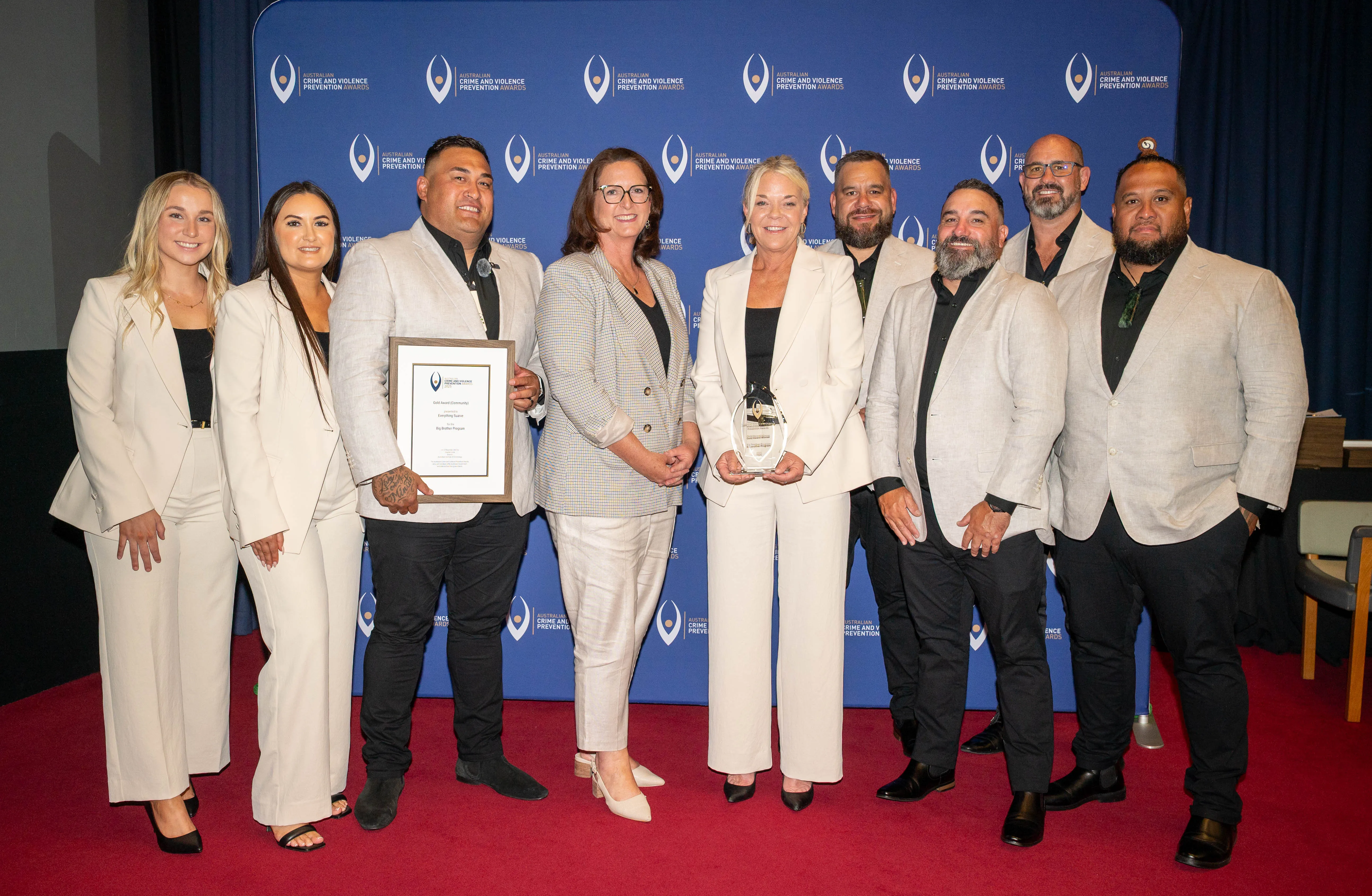 Nine people in light-colored suits posing with awards in front of Australian Crime and Violence Prevention banner.