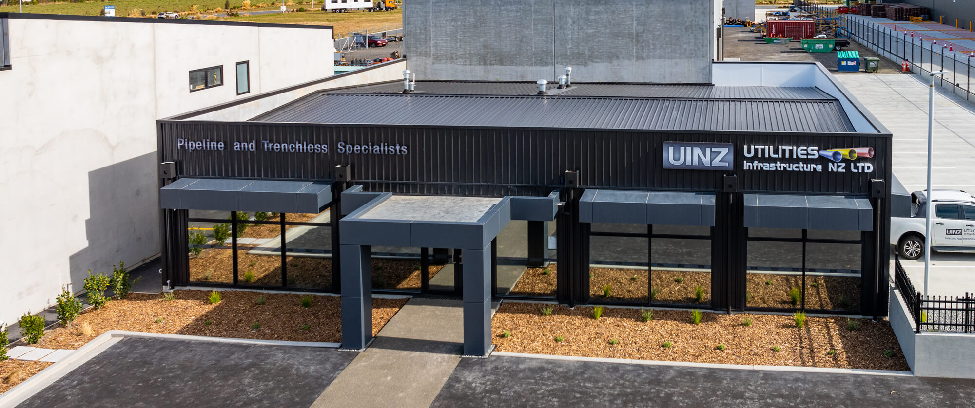 JLC Construction built this modern commercial building with black facade and signage for UINZ Utilities Infrastructure NZ LTD, showing entrance and landscaping.