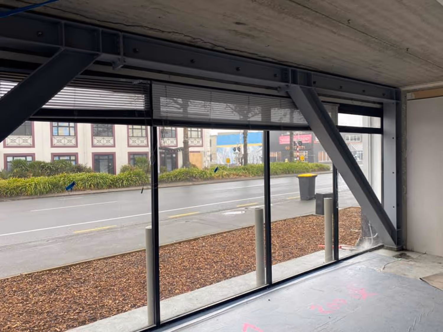 View from inside a building under JLC construction showing large glass windows with street view and a steel support beam.