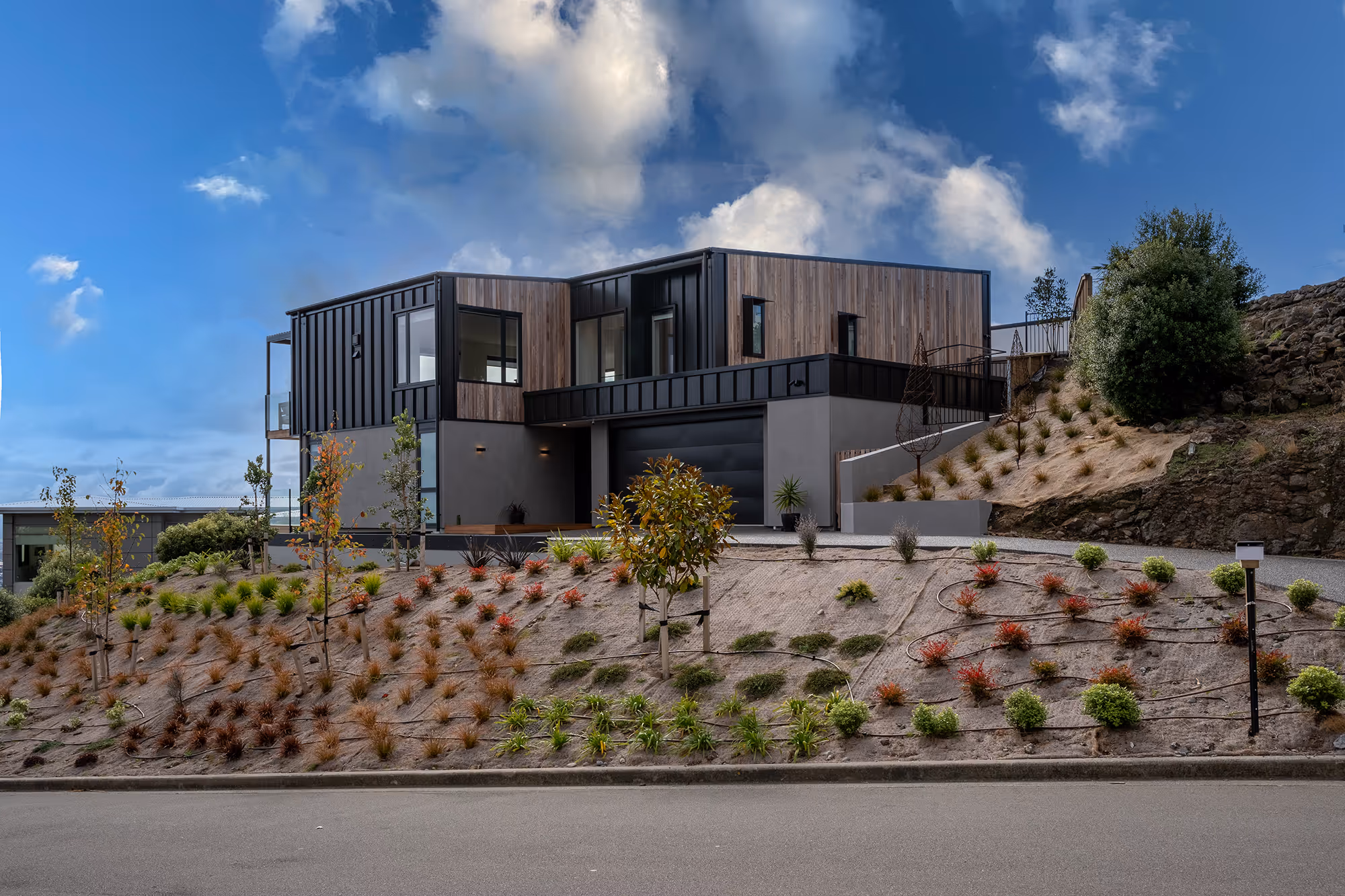 Bright living room with white couch, black pillows, wooden coffee table with white orchids, and sliding glass door opening to a small deck with chairs.