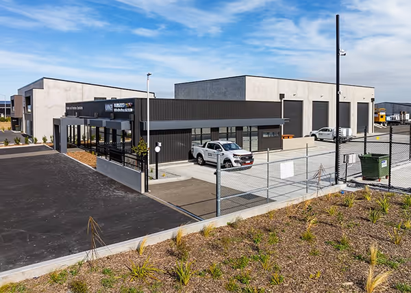 JLC Construction built this modern industrial building complex with black and gray exteriors, parking area with white trucks, under a partly cloudy sky.