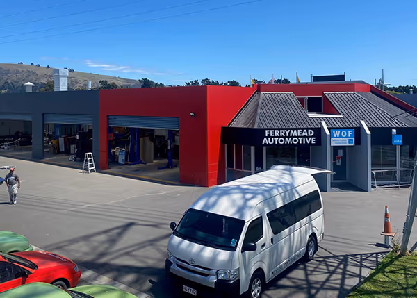 Exterior view of Ferrymead Automotive building with open garage bays, a white van, and a man walking nearby.