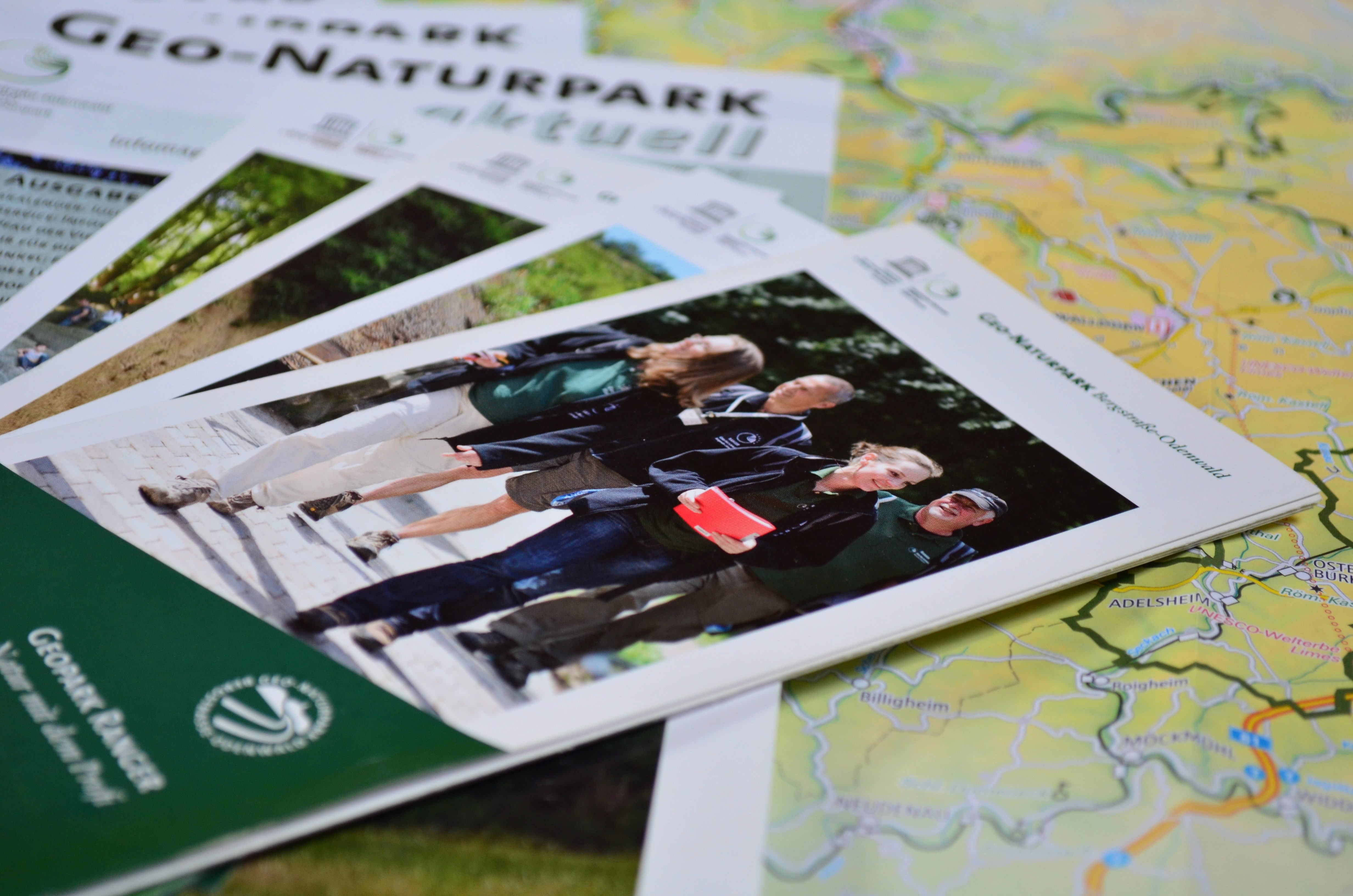 Broschüren mit Informationen zum Geo-Naturpark, darauf ein Foto von vier Menschen beim Wandern, arrangiert auf einer Landkarte.