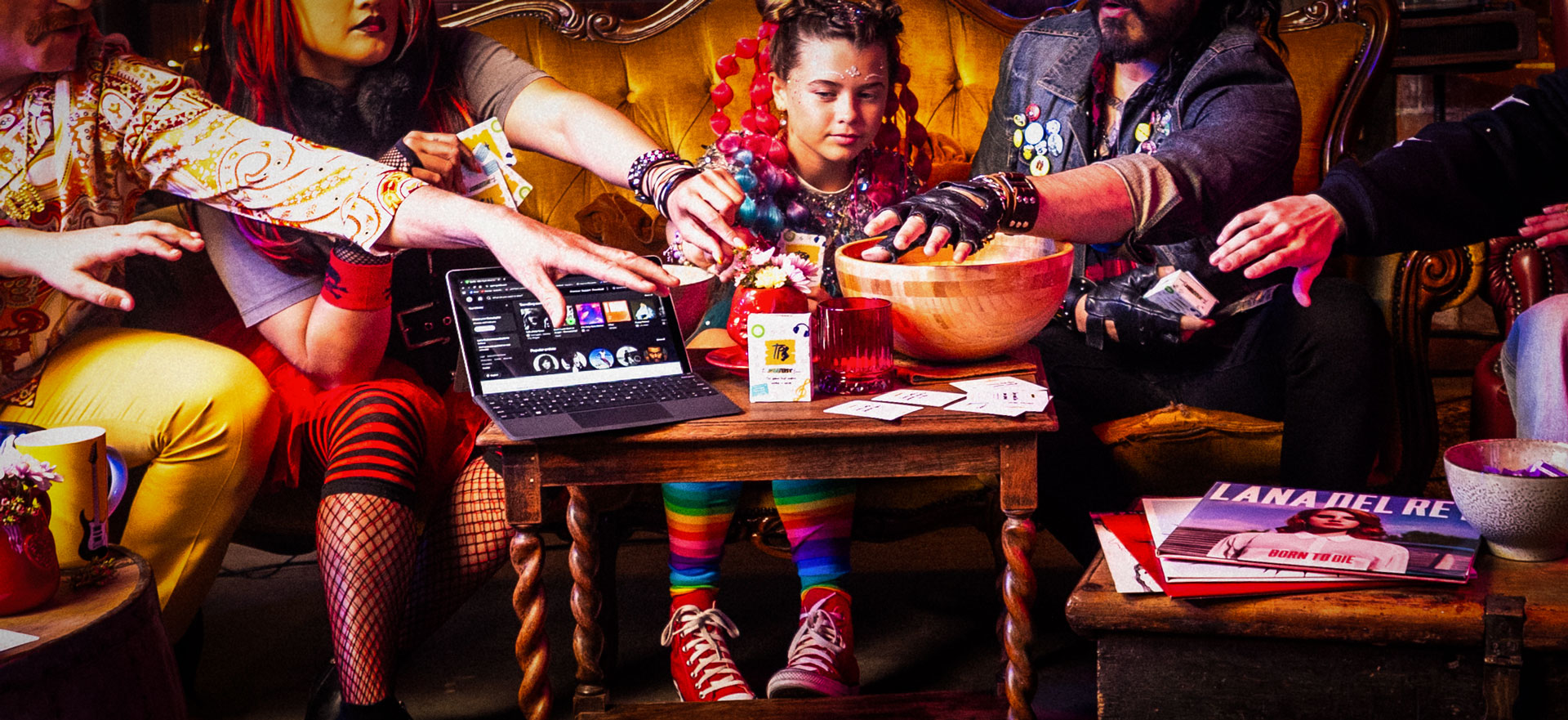 Group of people sitting on a couch reaching towards The Playlist Game, with a laptop with Spotify on the screen nearby.