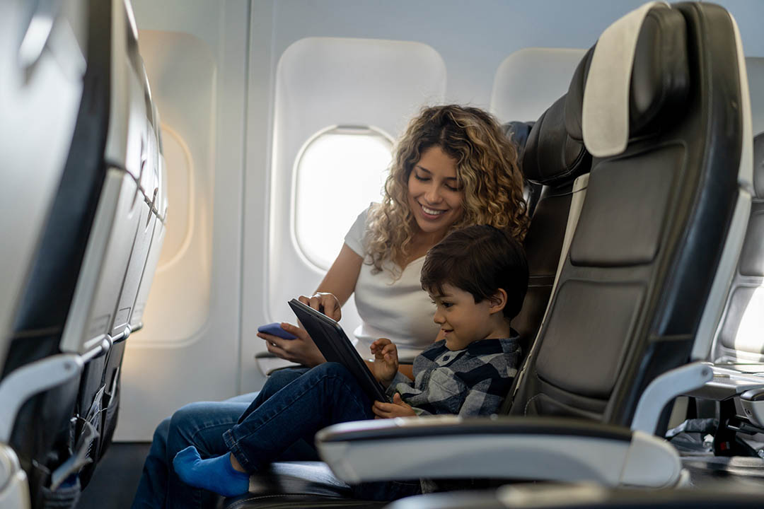 Smiling woman and young boy sitting side by side and using a tablet on an airplane.