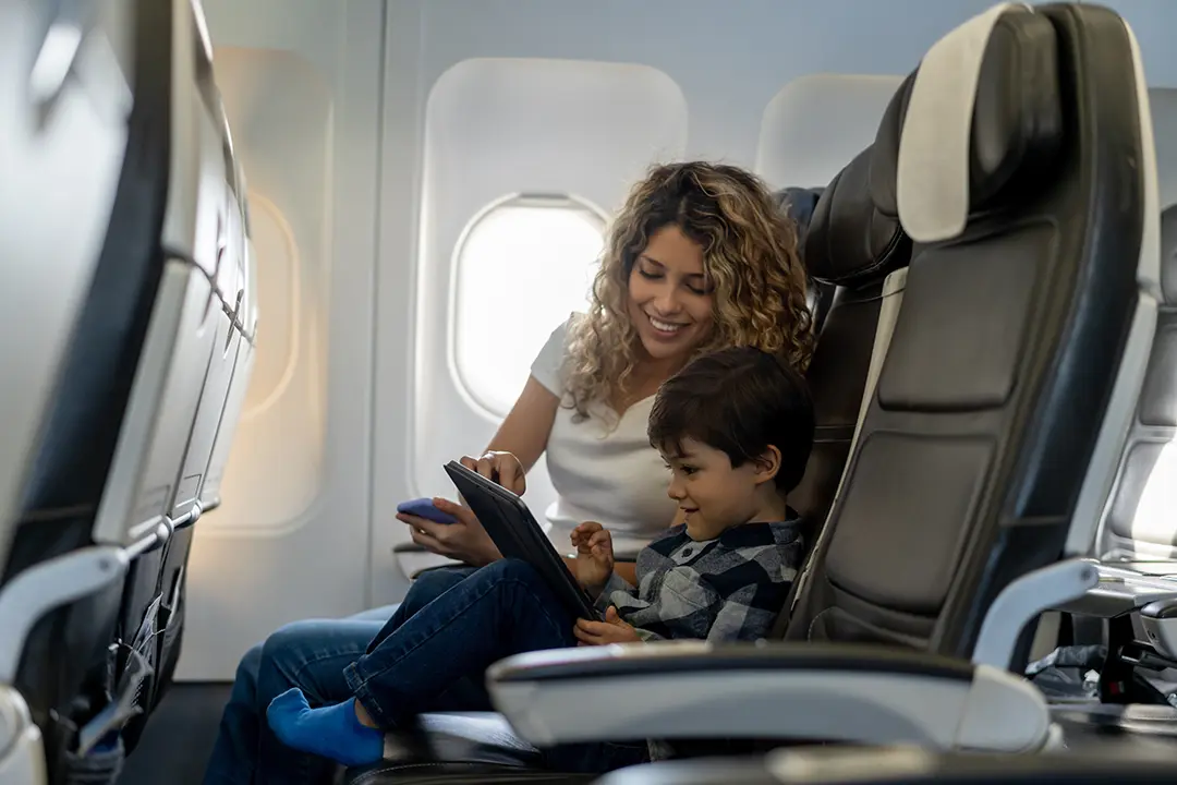 Smiling woman and young boy sitting side by side and using a tablet on an airplane.