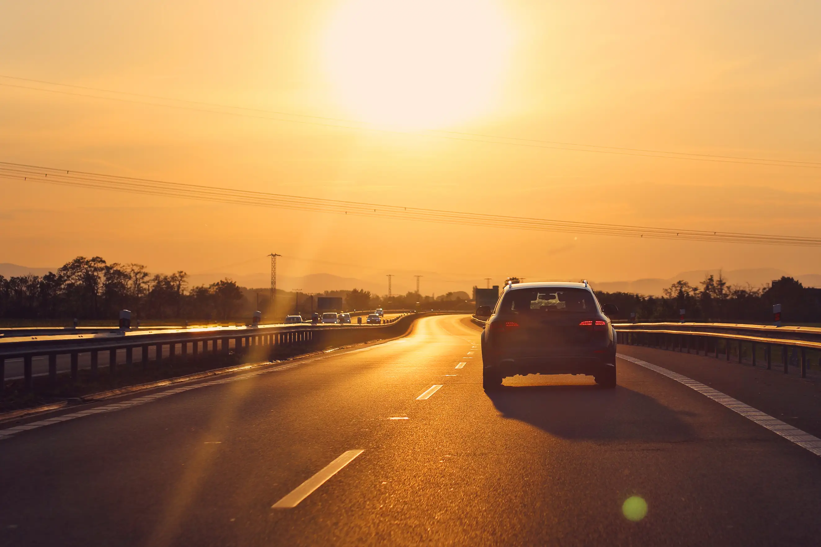 Auto fährt auf einer Autobahn bei Sonnenuntergang mit goldenem Licht.
