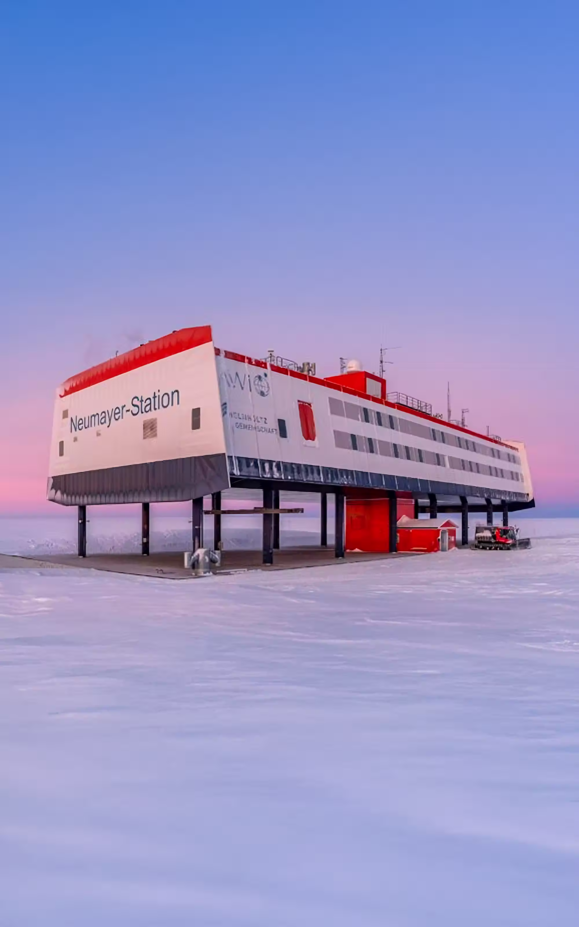 Neumayer-Station Forschungslaborgebäude auf Stelzen in verschneiter Antarktis bei Sonnenuntergang.